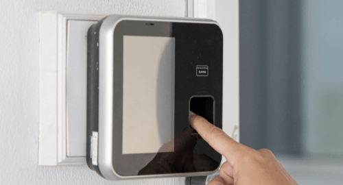 A person using a fingerprint scanner on a wall-mounted access control device.