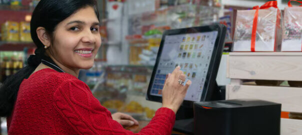 A smiling woman using a touchscreen POS system in a retail store.